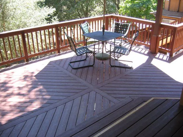 Outdoor deck with a square table, chairs, and umbrella. Wooden railing surrounds the space.