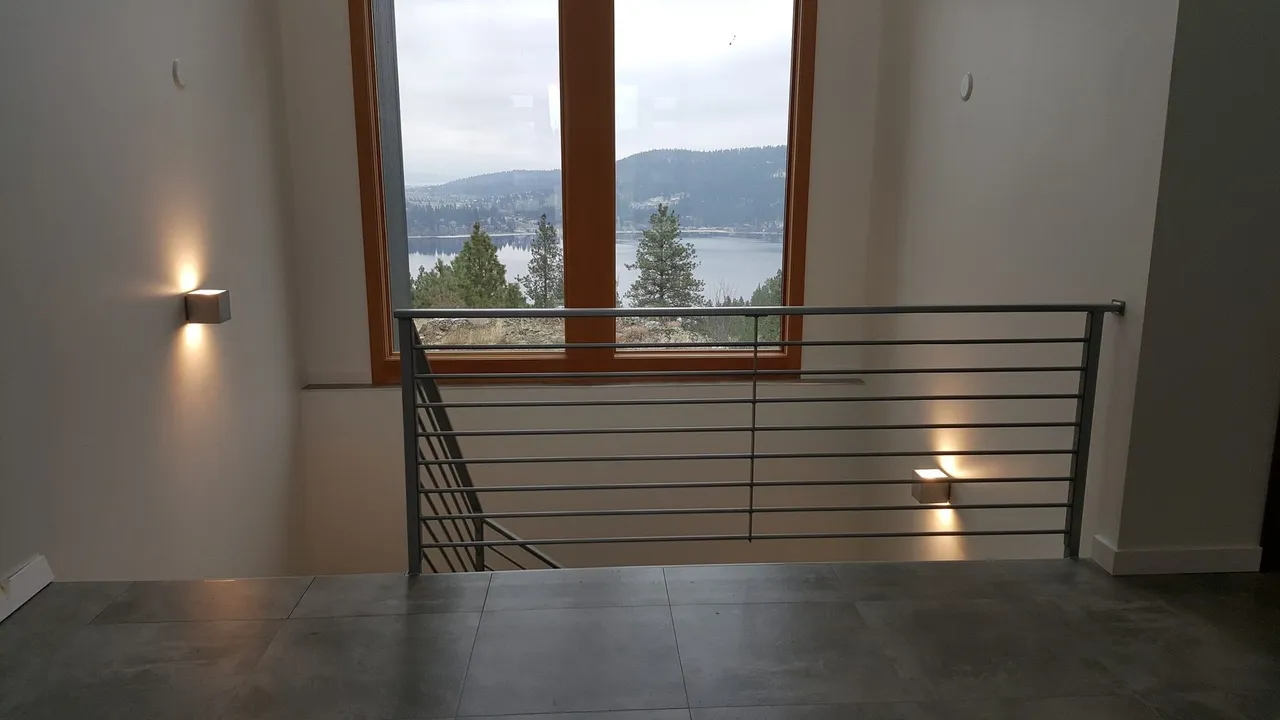 Interior view of a staircase with metal railing and window overlooking a lake and trees.