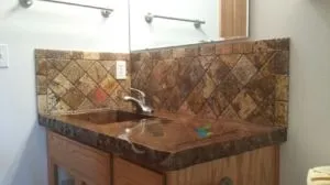Bathroom vanity with brown granite countertop and backsplash, wooden cabinet, and mirror.