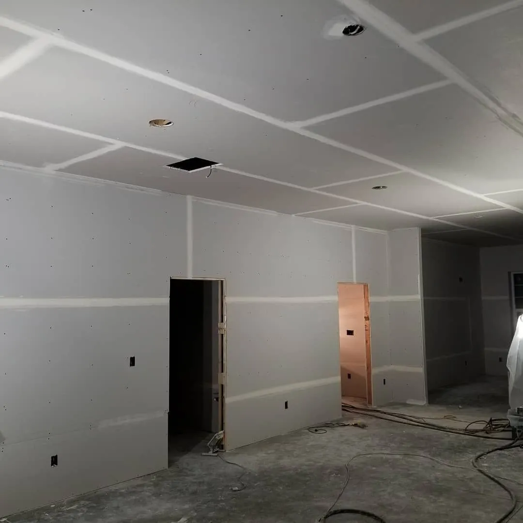 Interior of a room under construction with drywall on walls and ceiling, two doorways visible.