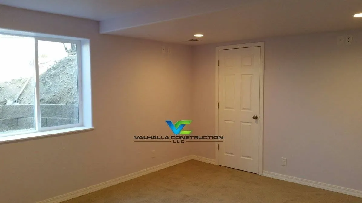 Empty room with window, door, beige walls, recessed lighting, and carpet.