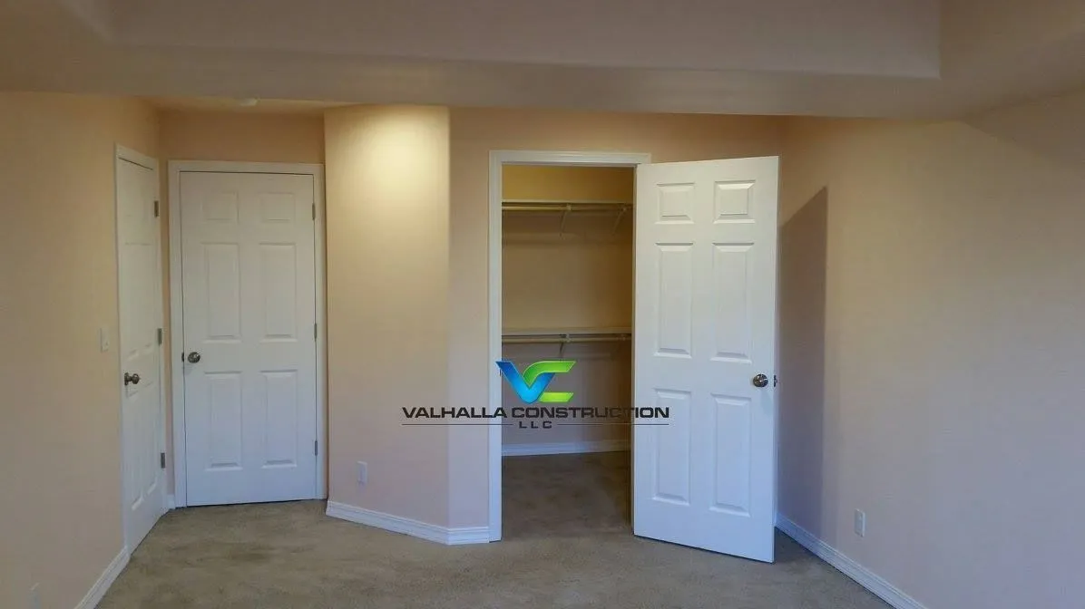 Beige bedroom with two white doors and an open closet.