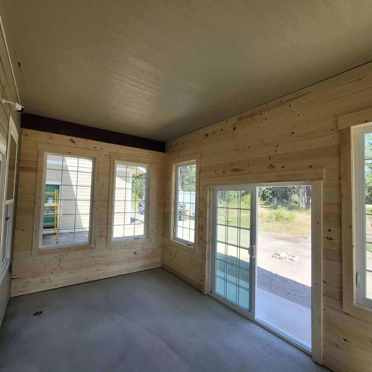 Empty room with light wood-paneled walls, a dark ceiling, and large windows and glass door.