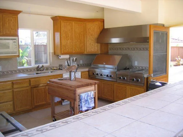 Outdoor kitchen with wooden cabinets, stainless steel grill, and tiled countertop.