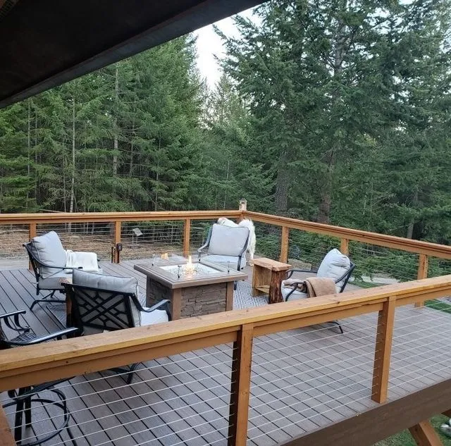 Outdoor deck with seating around a lit fire pit, trees in background.