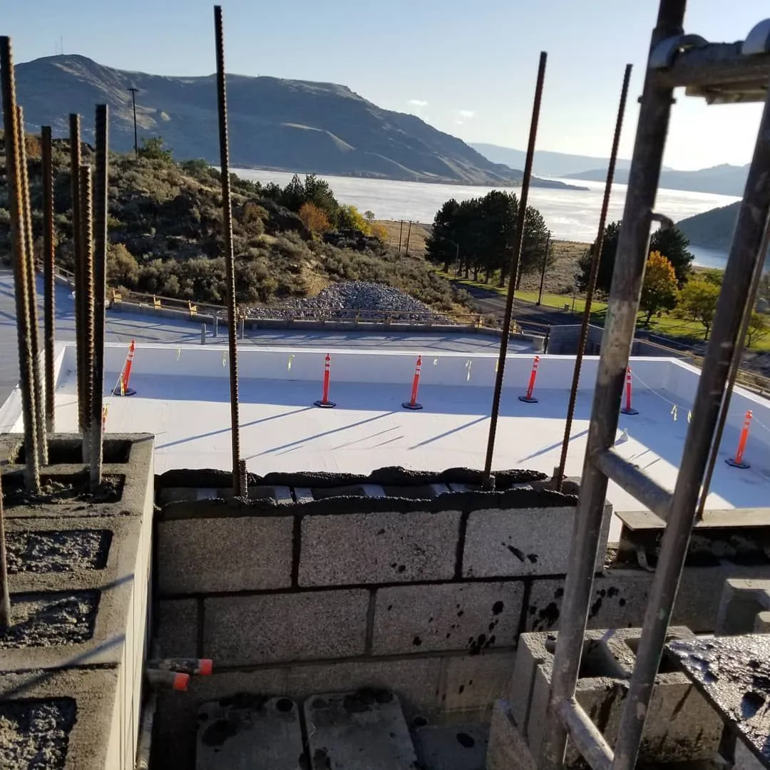 Construction of a concrete pool with rebar, cinder blocks, and a mountain and lake backdrop.
