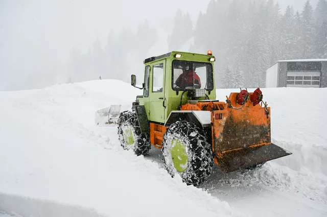 Orange snowplow clearing a snowy road in a heavy winter storm
