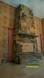 Stone fireplace under construction in a room, surrounded by unfinished walls with pink insulation.