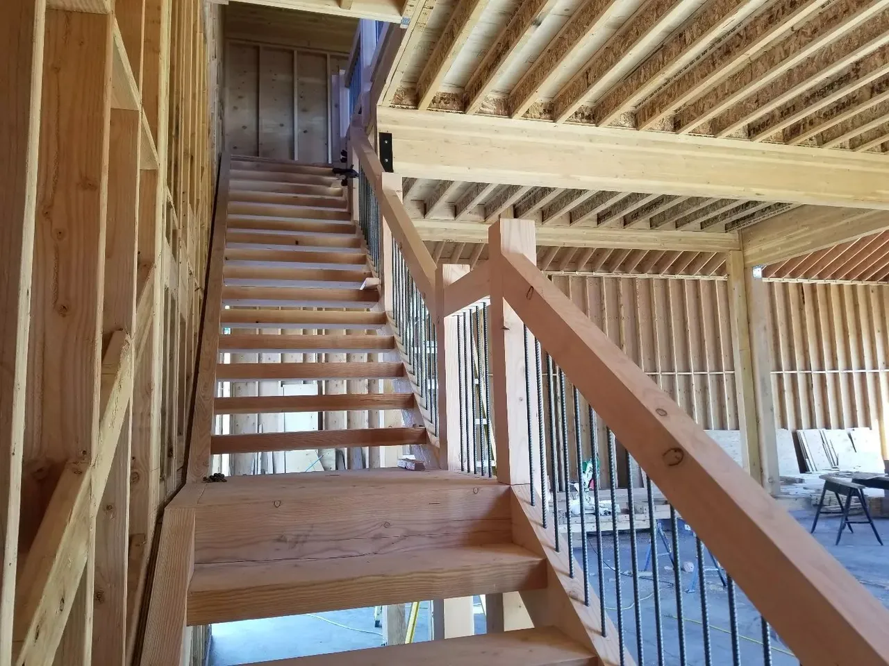 Wooden staircase inside an unfinished building with exposed framing and railing.