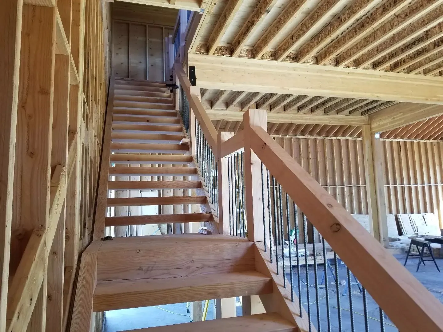 Wooden staircase inside an unfinished building with exposed framing and railing.
