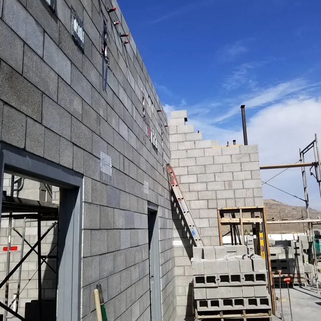 Building under construction with gray concrete block walls. Scaffolding, ladder, and blue sky visible.