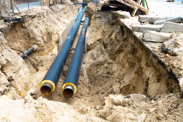 Two blue utility pipes laid in a dirt trench beside a stone walkway under construction.