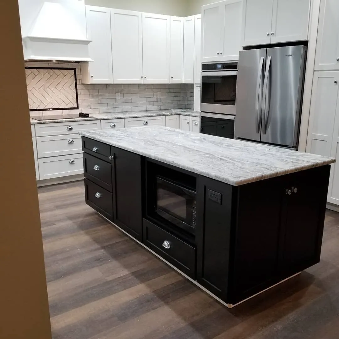 Kitchen with white cabinets, dark island with microwave, stainless steel refrigerator and light countertops.