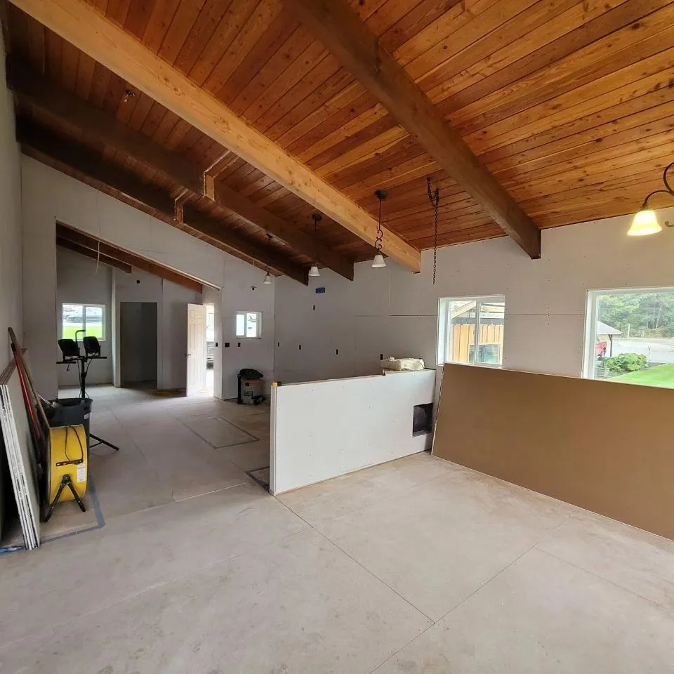 Interior view of a room under construction with wood ceiling beams, white walls, and concrete flooring.