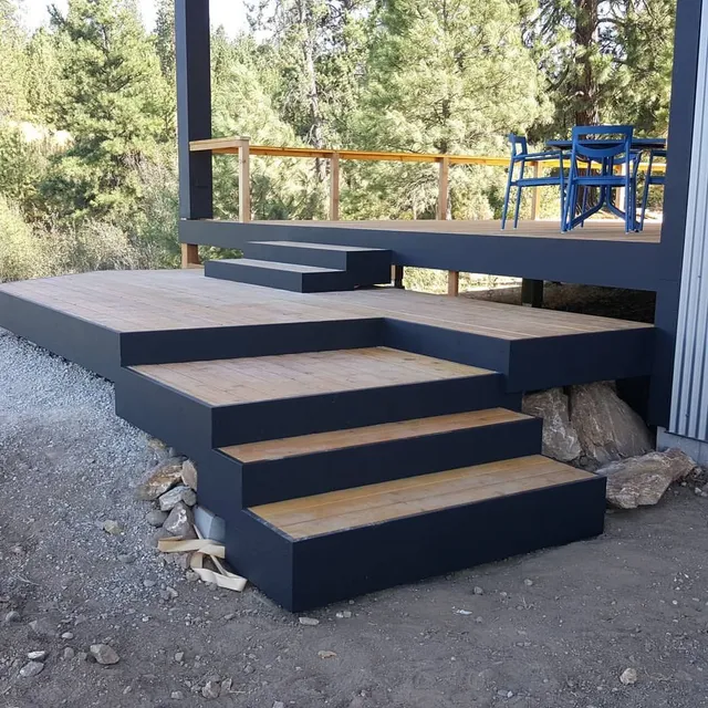 Outdoor deck with gray painted frame, wooden steps, and a blue table and chairs.
